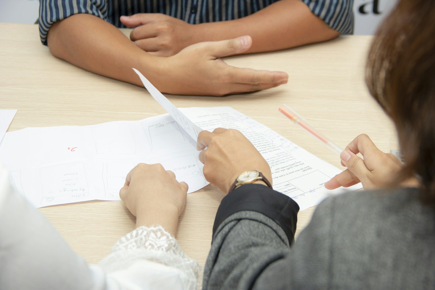 Three people reviewing printed documents together at a light wooden table