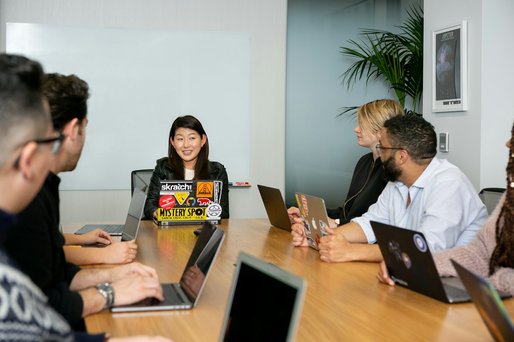 A small team around a wooden table with laptops, listening to one person speaking